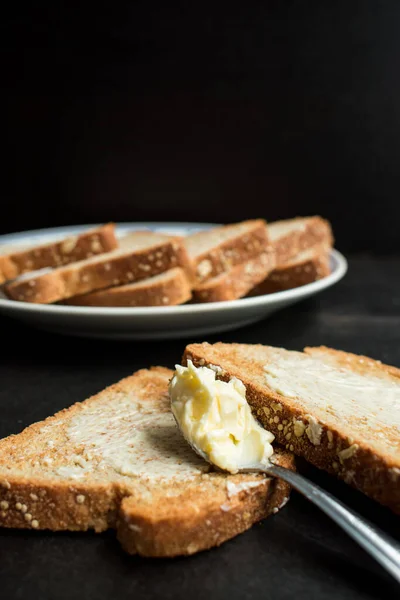一些全麦面包和黄油在盘子里的木制黑桌上 — 图库照片