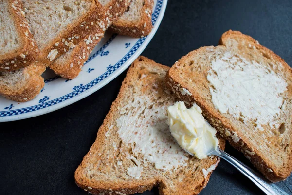 Algum Pão Integral Com Manteiga Uma Chapa Uma Mesa Escura — Fotografia de Stock