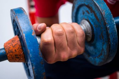 Spor salonunda egzersiz yapan genç bir adam tarafından kaldırılan eski mavi halterler.