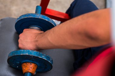 Spor salonunda egzersiz yapan genç bir adam tarafından kaldırılan eski mavi halterler.