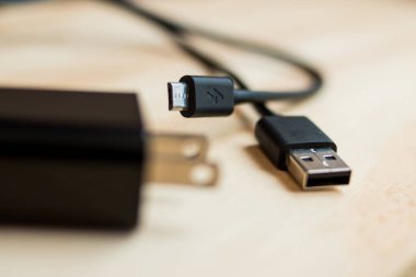 Siyah telefon şarj aleti ve USB kablosu ahşap bir masada.    