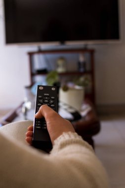 Evdeki siyah TV uzaktan kumandalı kanepede oturan kız.