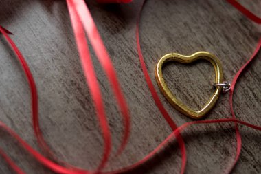 Tahta bir masada kırmızı kurdeleli altın çelik bir kalp.