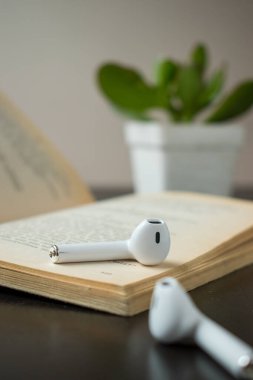 Siyah ahşap bir masanın üzerinde küçük bir bitki olan bir kitaptaki modern beyaz kulaklıklar. 