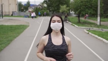 Spor pistinde gri eşofmanlı siyah saçlı atletik kız maske takıyor. Virüs ve enfeksiyonlara karşı korunma ve sağlık kavramı.