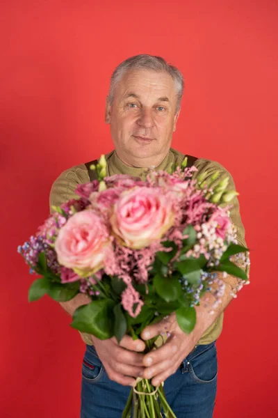 Пожилой человек с большим красивым букетом цветов стоит на красном фоне, концепция праздника и счастливой старости — стоковое фото