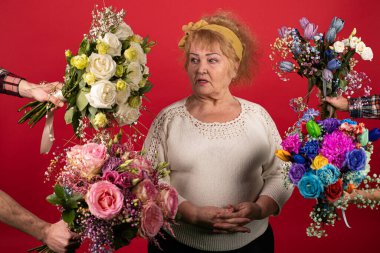 Yaşlı bir kadın çiçeklerle çevrilidir, mavi, sarı, beyaz, pembe - kadın bolluk ve renkler yüzünden kafası karışmıştır,