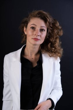 Beyaz takım elbiseli, siyah gömlekli, kendine güvenen kıvırcık saçlı genç bir kız.