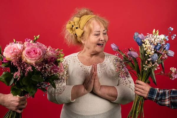 An elderly woman is presented with two bouquets of beautiful flowers at the same time, a woman delighted with an abundance of bright and fragrant surprises, positive emotions — Stock Photo, Image