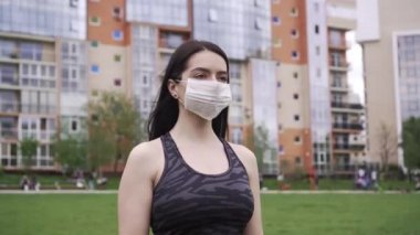 Siyah saçlı, gri üniformalı genç bir kız sokağın ortasında duruyor, önce tıbbi bir maske takıyor, sonra da virüslere karşı koruma kavramını ortadan kaldırıyor.