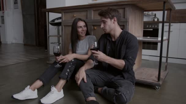 Хлопець і дівчина сидять на підлозі біля столу і п'ють вино, вони розважаються і сміються, концепція ізольованого життя — стокове відео