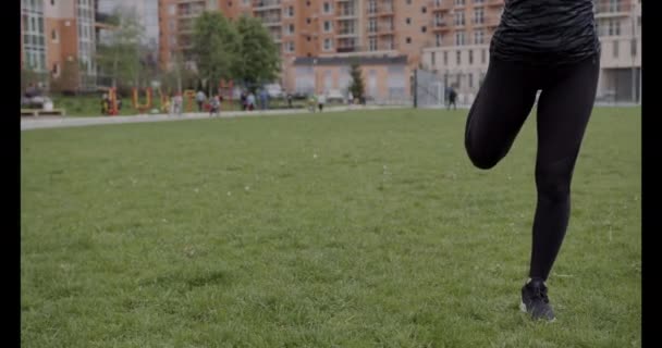 Close-up tiro, menina de tênis preto e leggings fazendo aquecimento na grama — Vídeo de Stock