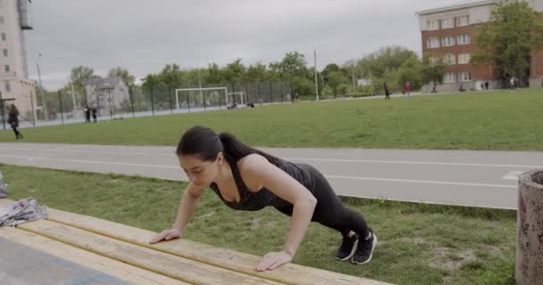 스포츠를 하는 여자 가 공원에 있는 벤치로 몰려오고 있습니다. 그녀는 집중적으로 숨을 쉬고 있고 열심히 노력하고 있습니다. — 비디오