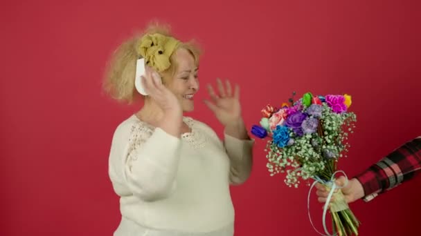 Улыбающаяся пожилая женщина слушает музыку и принимает цветы с улыбкой — стоковое видео