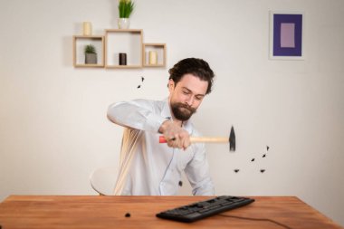 Agressive ofis çalışanı, sakallı kızgın adam bilgisayarını yok ediyor, elinde çekiçle klavyeyi yok ediyor..