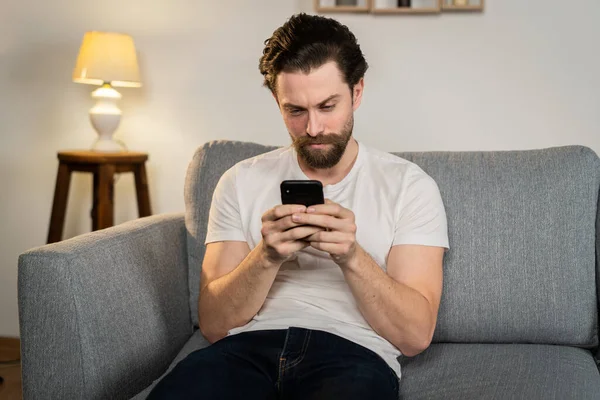 Genç bir adam evde tek başına oturuyor, sosyal medyada geziniyor, izole edilmiş, haberleri okuyor.