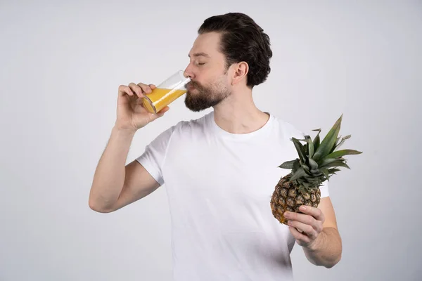 O homem com barba longa segura o abacaxi nas mãos e bebe o suco dele. Dieta e fitness. Olha para a câmara. — Fotografia de Stock