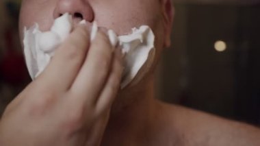 Yetişkin bir adam sakalını kesmek için yüzüne köpük sürmüş. Coronavirus salgını, evde kal..