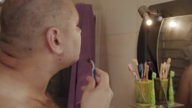 Yetişkin bir adam, Cavid-19 kapanırken sakalını kesmek için bıçak kullanır. Aynaya bak. Coronavirus salgını, evde kal..