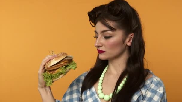 Pin up mujer mirando hamburguesa y encoge de hombros sobre fondo amarillo — Vídeos de Stock