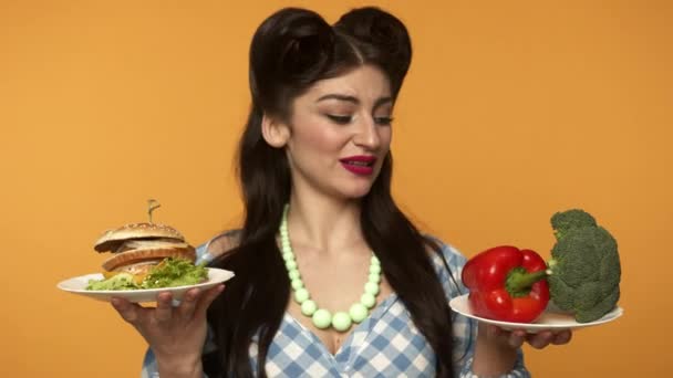 Mosolygós pin up nő néz tányérok és nem tud választani a gyorsétterem és zöldség — Stock videók