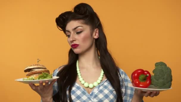 Insatisfeito pin up mulher segurando hambúrguer e comida vegetariana — Vídeo de Stock