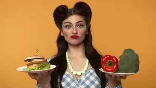 Éhes pin up nő nézi burger és zöldségek mosollyal — Stock videók