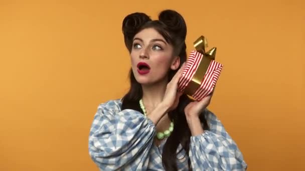 Curiosa pin up chica sosteniendo caja de regalo y sonriendo a la cámara — Vídeo de stock