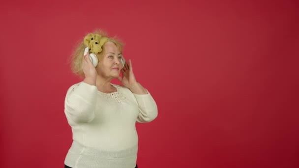 Starší žena s nadváhou tančí při poslechu hudby ve sluchátkách, usmívá se a bere květiny od vnuka — Stock video
