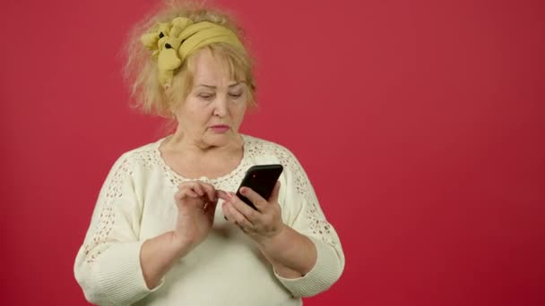 Mujer mayor con sobrepeso escribiendo en el teléfono inteligente con sonrisa en el fondo rojo — Vídeo de stock