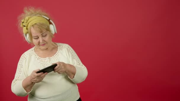 Mulher com sobrepeso sênior em fones de ouvido jogando no smartphone — Vídeo de Stock