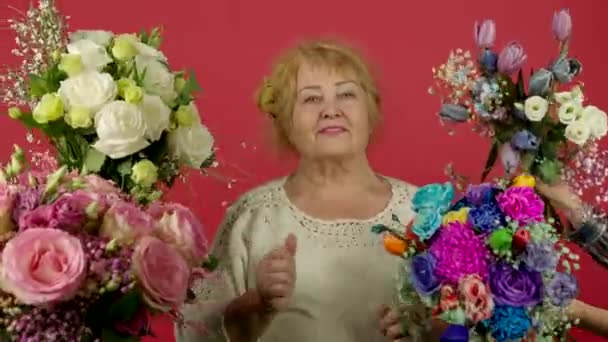 Gülümseyerek çiçeklerin yanında dans eden neşeli yaşlı kadın. — Stok video