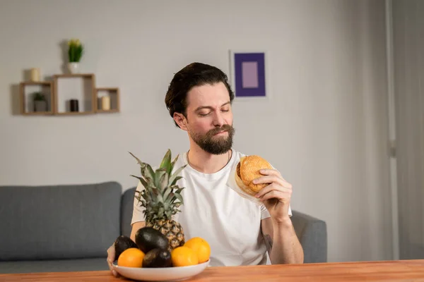 Um jovem senta-se à mesa e fala sobre a utilidade dos frutos, pega neles e mostra laranja — Fotografia de Stock