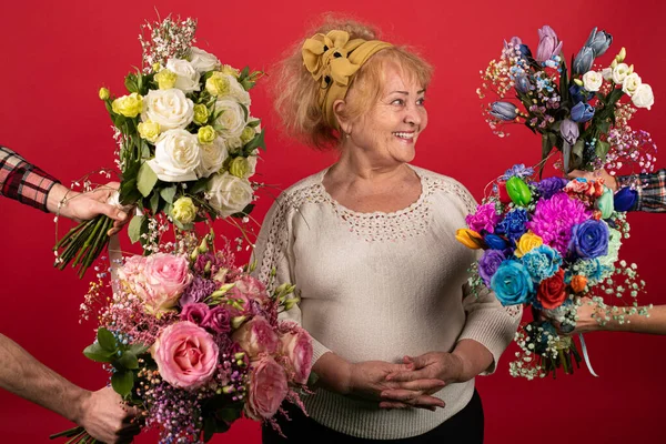 Yaşlı bir kadın çiçeklerle çevrilidir, mavi, sarı, beyaz, pembe - bolluk ve renklerle mutlu bir kadın