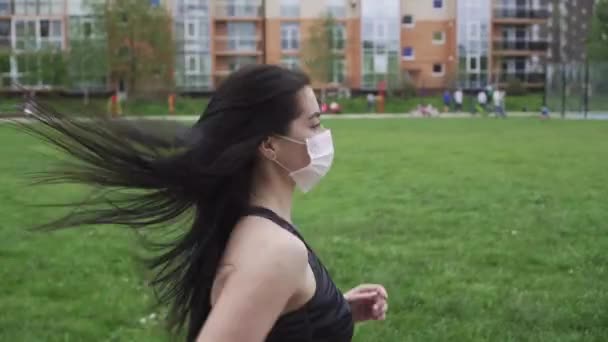 Sportos lány sötét hajjal, szürke melegítőben egy sportpályán Maidan fut, maszkban van, az egészség és a vírusok elleni védelem koncepciójában. — Stock videók