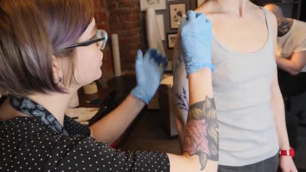 Tattoo umělec v práci. Dívka drží tetování stroj a použité ve vzorci na kůži. Modrý inkoust v tetování stroj.