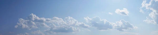 White fluffy clouds on a gentle blue sky in the rays of the sun. Panoramic view. Abstract blue sky background. Clouds in the sunlight.