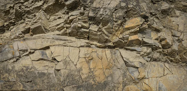 Rock texture. Stone background. Old weathered crumbling mountain surface in cracks background. Light brown rock background.