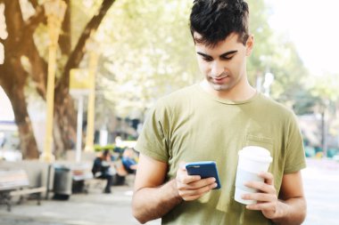 Holding kahve ve okuma iletisi yaptığı telefon genç adam. Açık havada.