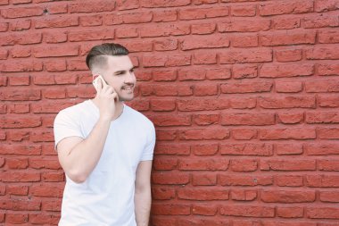 Duvara karşı telefonda konuşan genç latin adam portresi. Açık havada.