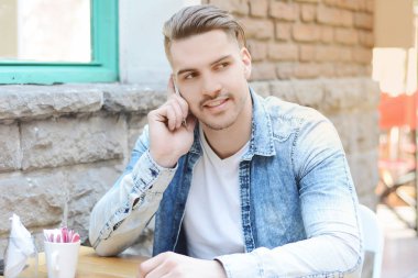 Genç adam telefonda konuşurken kafede. Açık havada