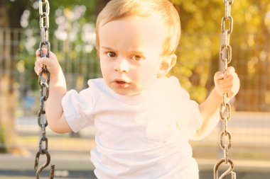 Şirin bebek çocuk bir parkta bir salıncak üzerinde eğleniyor.