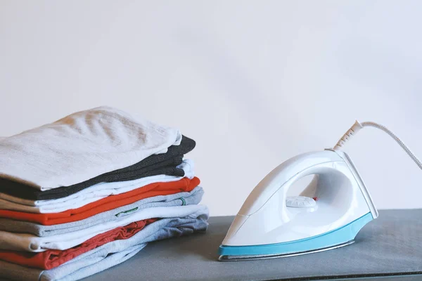 Close up view of iron clothes on ironing board with stack of ironed shirts. Housework concept