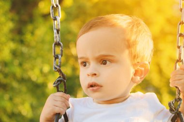 Şirin bebek çocuk bir parkta bir salıncak üzerinde eğleniyor.