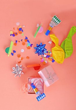 Red gift box with party confetti, streamers and noisemakers on orange background. Celebration concept clipart