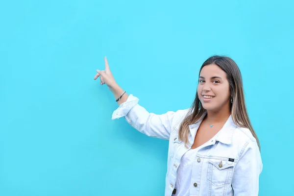 微笑的年轻女子的肖像 指向在浅蓝色墙壁上的复制空间 广告理念 — 图库照片