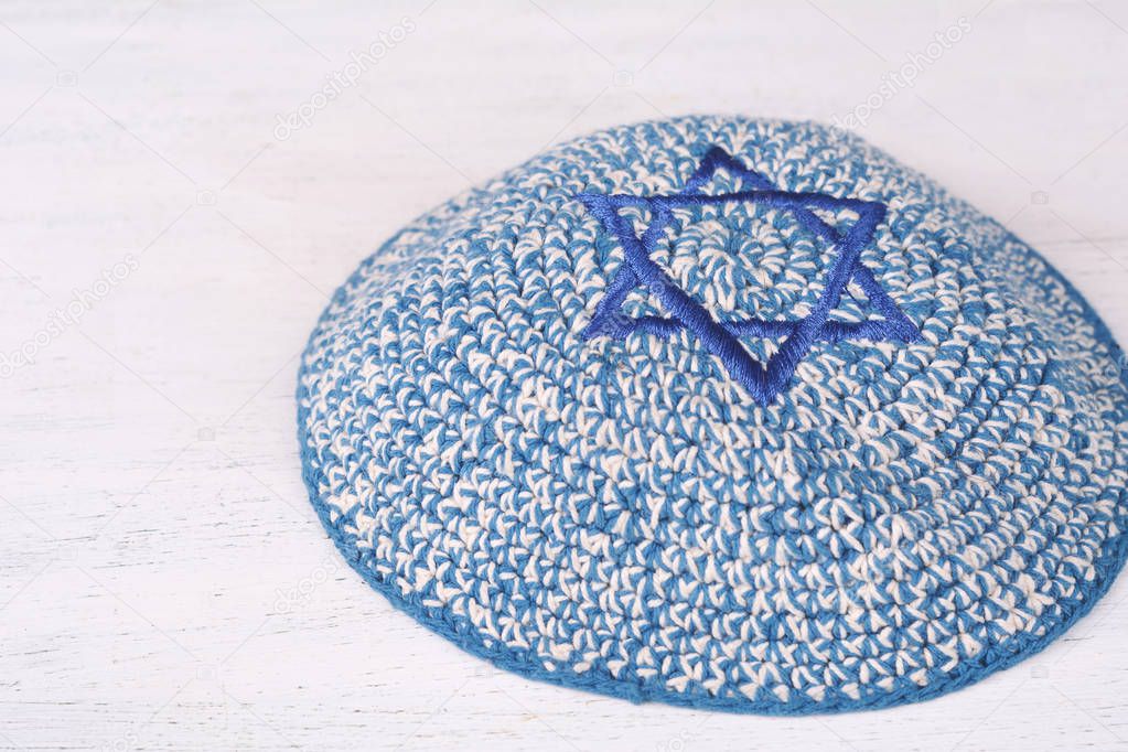Knitted kippah with embroidered blue star of david with copy space on a wooden table. Jewish lifestyle concept 
