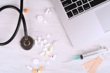 Üstten Görünüm dizüstü bilgisayar, not defteri, stetoskop, ilaç şişeleri ve şırınga doktorun masasından. Modern tıp işyeri 
