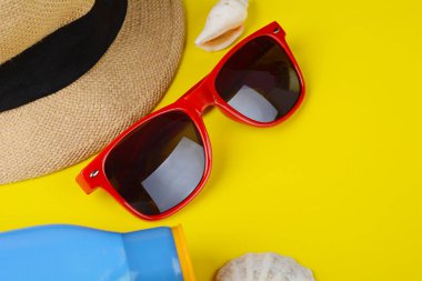 Sarı zemin üzerine üstten görünüm güneş gözlüğü, kabukları, deniz yıldızı ve güneş kremi. Yaz konsepti.