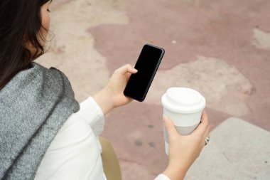 Kağıt bardak kahve içme ve bir onu kullanarak güzel kadın kış sokakta telefon. Concep götür